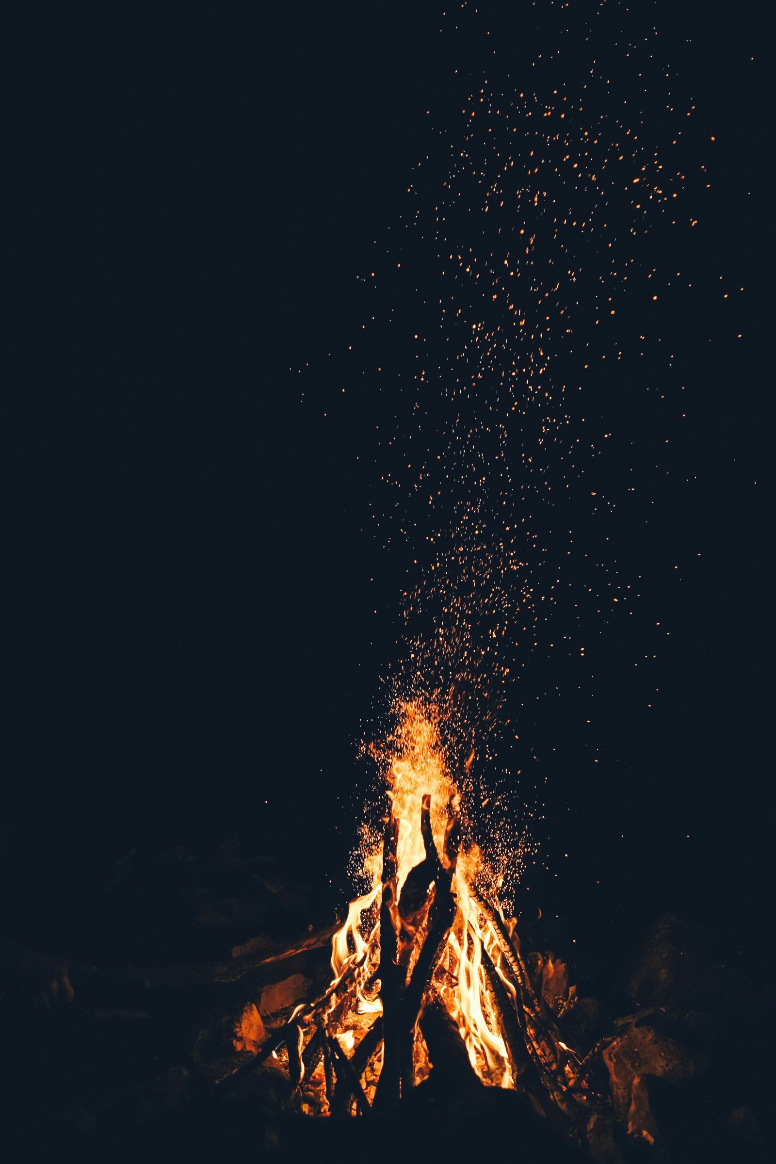 A campfire burning at night, sending a column of sparks up into the dark